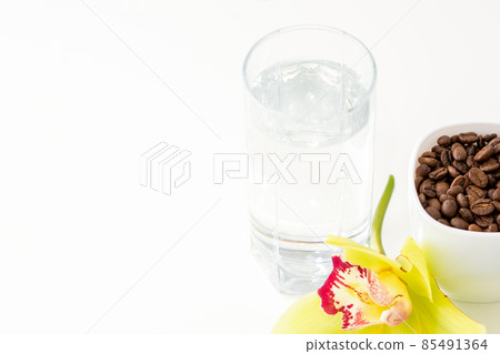 Cup of coffee beans and glass of water with yellow orchid flower against a white background. Cup of coffee beans and glass of water with yellow orchid flower against a white background. 85491364
