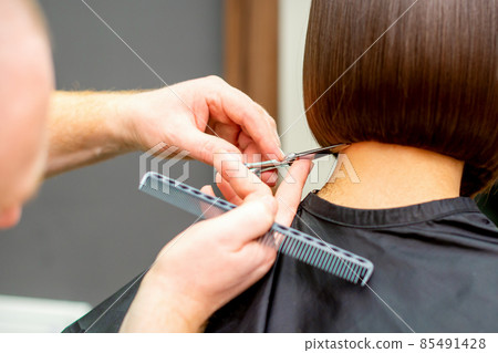 The hairdresser cuts the hair of a brunette woman. Hairstylist is cutting the hair of female client in a professional hair salon, close up. The hairdresser cuts the hair of a brunette woman. Hairstylist is cutting the hair of female client in a professional hair salon, close up. 85491428