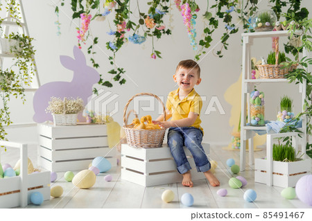 Happy boy holds the basket with fluffy ducklings while sits on the wooden box. Easter decoration. Happy boy holds the basket with fluffy ducklings while sits on the wooden box. Easter decoration. 85491467