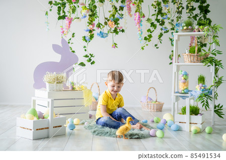 Smiling child sits on wooden floor with little duckling in Easter decoration. Easter for children 85491534