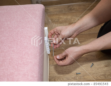 The process of assembling upholstered furniture. A man screwing the armrest mountings with a hex screwdriver 85491543