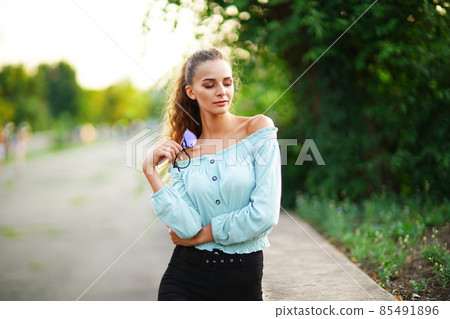 stylish beautiful young woman wears in summer bright hipster clothes while posing in the park 85491896