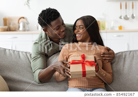 Loving african american man hugging his wife, giving present Loving african american man hugging his wife, giving present 85492167