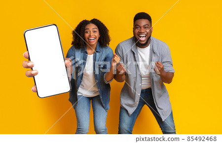 Black couple showing white empty smartphone screen and gesturing yes Black couple showing white empty smartphone screen and gesturing yes 85492468