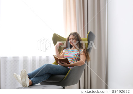 Young woman reading book in armchair at home 85492632