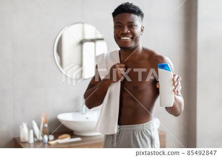 Cheerful African American Guy Showing Shower Gel Bottle In Bathroom 85492847