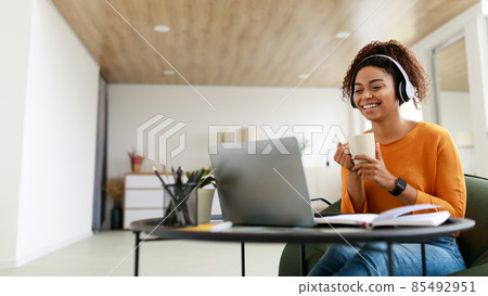 Smiling black lady watching video on computer, drinking hot coffee Smiling black lady watching video on computer, drinking hot coffee 85492951