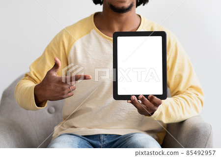 Black Guy Pointing At Digital Tablet With Blank Screen, Sitting In Armchair 85492957