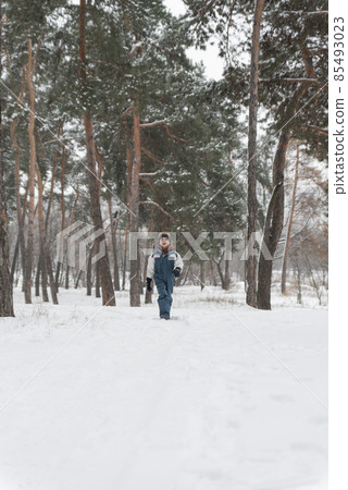 Boy in winter jumpsuit and multi-colored hat comes out snow-covered forest. Walk against of beautiful winter landscape Boy in winter jumpsuit and multi-colored hat comes out snow-covered forest. Walk against of beautiful winter landscape 85493023
