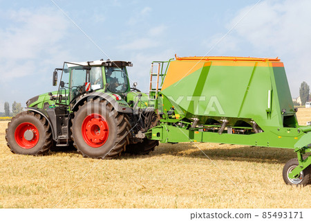 The versatile seed drill is mounted on a tractor against the backdrop of a harvested agricultural field. 85493171