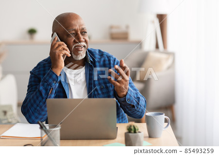 Senior African Businessman Talking On Phone Sitting At Laptop Indoor Senior African Businessman Talking On Phone Sitting At Laptop Indoor 85493259