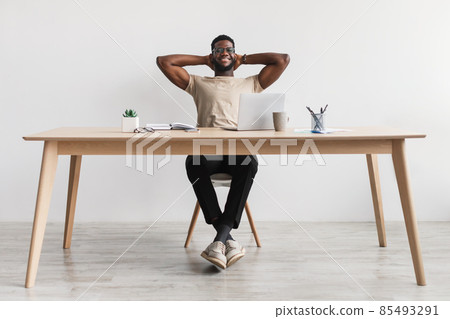 Happy millennial black man relaxing after work, putting feet on table at home office, full length Happy millennial black man relaxing after work, putting feet on table at home office, full length 85493291