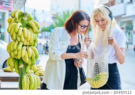 Mother and teenage daughter buying bananas at a street retail market 85493512