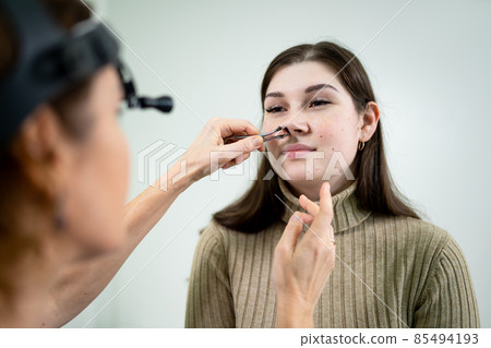 Professional female doctor otorhinolaryngologist doing nose examination with otoscope in modern hospital. Nasal congestion, sinusitis, allergy concept. Woman ENT doctor and patient in office clinics Professional female doctor otorhinolaryngologist doing nose examination with otoscope in modern hospital. Nasal congestion, sinusitis, allergy concept. Woman ENT doctor and patient in office clinics 85494193