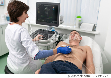 Woman doctor makes heart check of patient man using modern equipment in a cardiology clinic. Female cardiologist is screaning patient heart with ultrasonography, looking at screen. Healthcare concept Woman doctor makes heart check of patient man using modern equipment in a cardiology clinic. Female cardiologist is screaning patient heart with ultrasonography, looking at screen. Healthcare concept 85494273