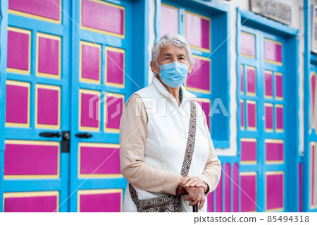 Senior woman wearing a face mask at a traditional colorful street in the beautiful colonial town of Salento in the region of Quindio in Colombia 85494318