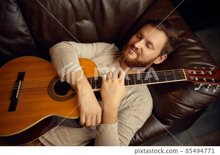 Young man lying on couch with guitar Young man lying on couch with guitar 85494771