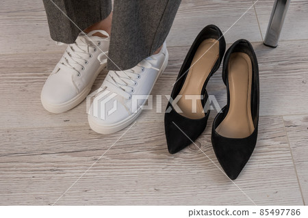 Close-up business woman takes off her shoes puts on white leather sneakers. 85497786