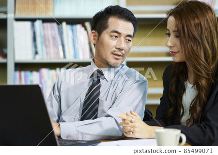 asian businessman and businesswoman having a discussion in office using laptop computer 85499071