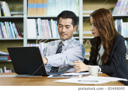 asian businessman and businesswoman having a discussion in office using laptop computer 85499095