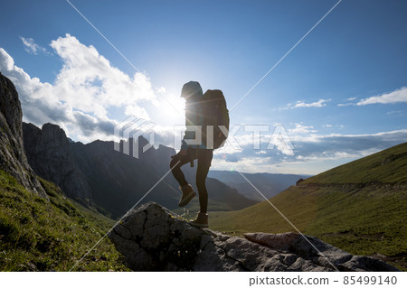 Successful woman backpacker hiking on sunset alpine mountain peak Successful woman backpacker hiking on sunset alpine mountain peak 85499140