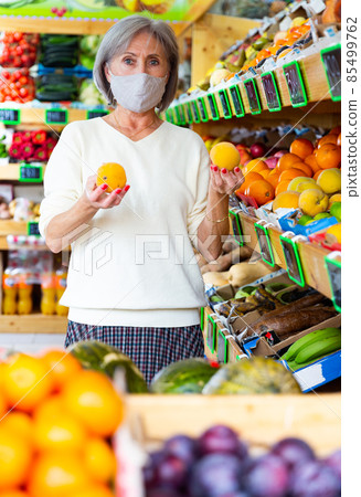 Woman in protective mask choosing sweet tangerines and other fruit on counter of market Woman in protective mask choosing sweet tangerines and other fruit on counter of market 85499762