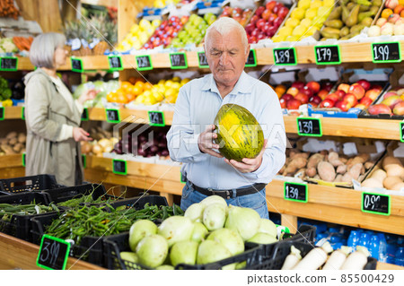Portrait of adult man choosing fresh ripe watermelon from counter at farmers market 85500429