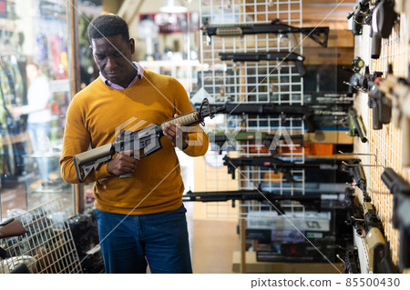 Portrait of african american man choice pneumatic gun in airsoft market Portrait of african american man choice pneumatic gun in airsoft market 85500430