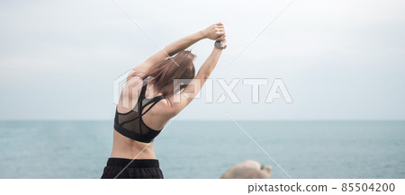 Young fitness female in sportswear stretching body against ocean view, healthy woman exercise in morning. Workout, wellness and work life balance concepts 85504200