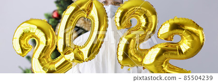 Woman in protective suit and mask holds numbers 2022 against background of Christmas tree Woman in protective suit and mask holds numbers 2022 against background of Christmas tree 85504239