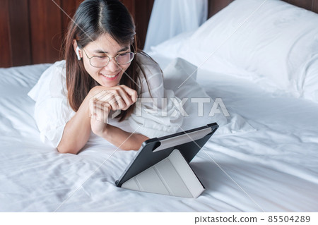 Happy woman using tablet for social media, young female watching movies on computer pad on bed at home. technology, network, online shopping, e commerce, lifestyle and digital communication concept Happy woman using tablet for social media, young female watching movies on computer pad on bed at home. technology, network, online shopping, e commerce, lifestyle and digital communication concept 85504289