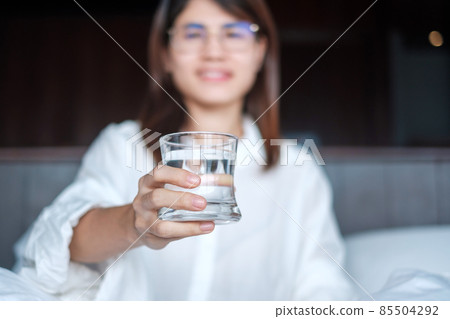Happy woman holding water glass, female drinking pure water on bed at home. Healthy, Refreshment, lifestyle concept Happy woman holding water glass, female drinking pure water on bed at home. Healthy, Refreshment, lifestyle concept 85504292