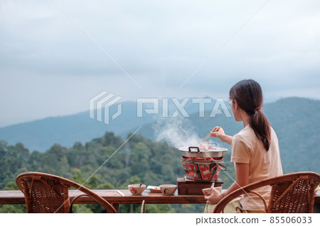 Woman grill Pork or meat with vegetables and soup on the hot pan against mountain view background, Traditional Thai BBQ style is famous in Thailand 85506033