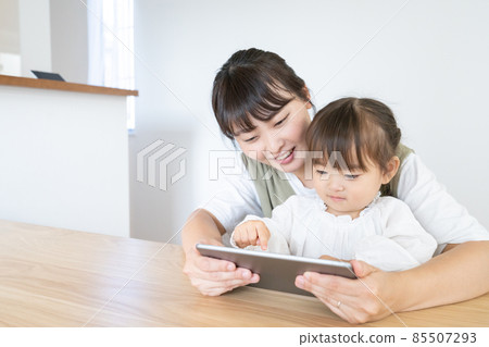 A 2-year-old girl looking at a tablet with her mom in the dining room at home A 2-year-old girl looking at a tablet with her mom in the dining room at home 85507293