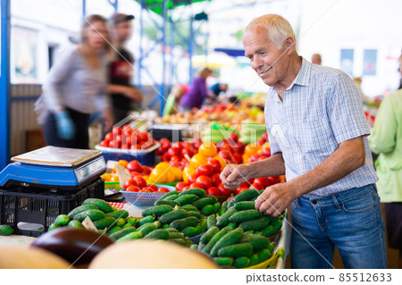 retired european man buys cucumbers and tomatoes in market 85512633