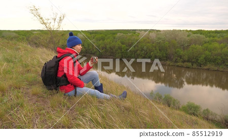 The girl drinks tea from a mug sitting on a high mountain and enjoying nature in the park. Woman traveler looking for adventure. Relax on the hike. Long distance hiking trips. Human explorer of 85512919