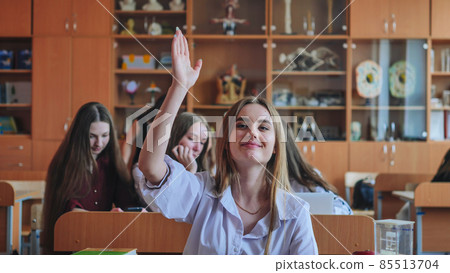 A girl student sitting at a desk raises her hand in the class. 85513704