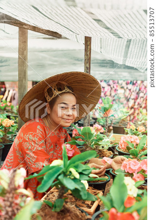 Happy asian woman with Vietnamese straw hat potting flowers in her garden 85513707