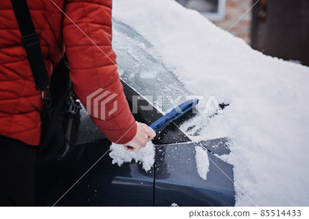 Man cleaning car from snow and ice with brush and scraper tool during snowfall. Winter emergency. Weather-related vehicle emergencies. Automobile covered with snow 85514433