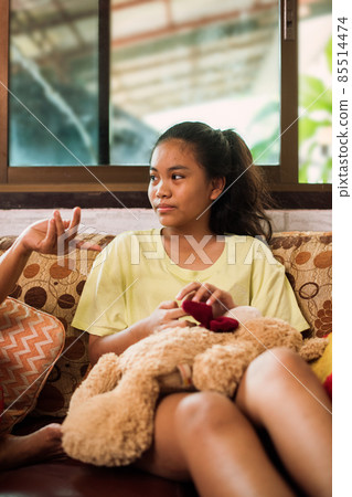 Thai teenager girl sitting on couch with mobile phone and looking to window. Thai teenager girl sitting on couch with mobile phone and looking to window. 85514474