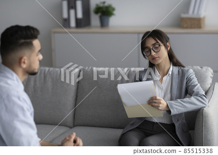 Psychotherapy concept. Focused female psychotherapist interviewing young man, listening and taking notes Psychotherapy concept. Focused female psychotherapist interviewing young man, listening and taking notes 85515338