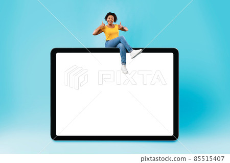 Cool young black woman sitting on giant cellphone, showing thumb up gesture, recommending new app or website, mockup 85515407
