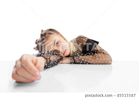 Close-up beautiful little cute girl, pupil in black dress sitting at table isolated on white studio background. Education, childhood concept. Close-up beautiful little cute girl, pupil in black dress sitting at table isolated on white studio background. Education, childhood concept. 85515587
