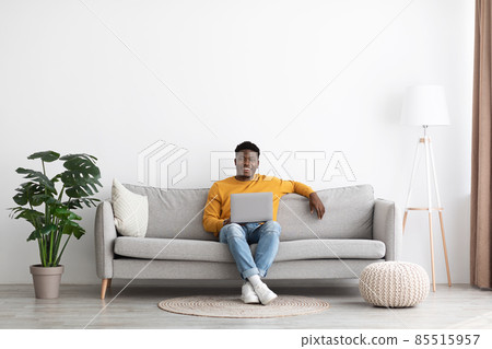 Smiling black guy chilling with laptop at home 85515957