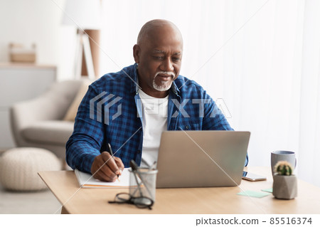 Senior Black Man Using Laptop Taking Notes Working At Home 85516374