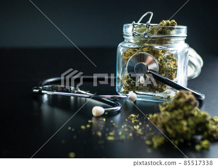 Dry medical cannabis in a jar with a stethoscope on a black background Dry medical cannabis in a jar with a stethoscope on a black background 85517338