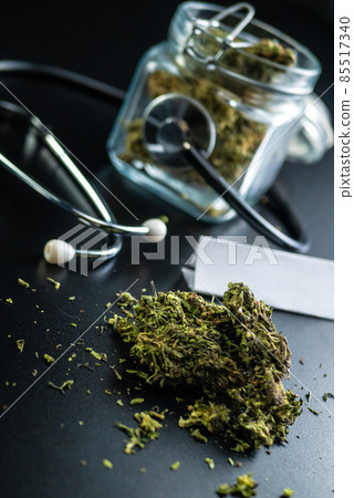 Dry medical cannabis in a jar with a stethoscope on a black background Dry medical cannabis in a jar with a stethoscope on a black background 85517340