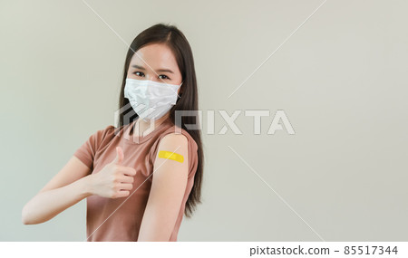 asian female thumbs up wearing mask with showing plaster on shoulder after covid-19. asian female thumbs up wearing mask with showing plaster on shoulder after covid-19. 85517344