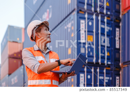 man engineering in uniform wearing safety helmet using laptop checking containers loading. man engineering in uniform wearing safety helmet using laptop checking containers loading. 85517349