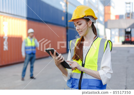 Women worker use tablet in uniform wearing safety helmet using laptop checking containers loading. Women worker use tablet in uniform wearing safety helmet using laptop checking containers loading. 85517350